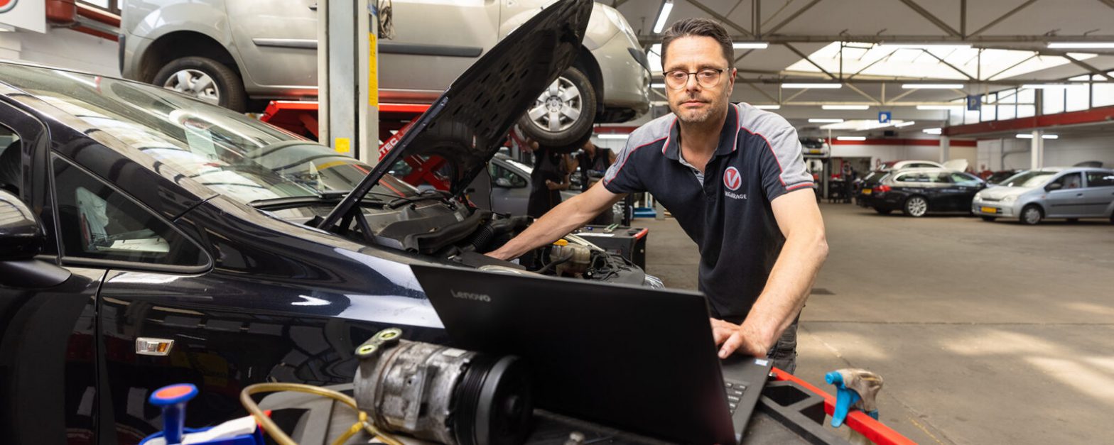 Foto van een automonteur die op zijn laptop kijkt